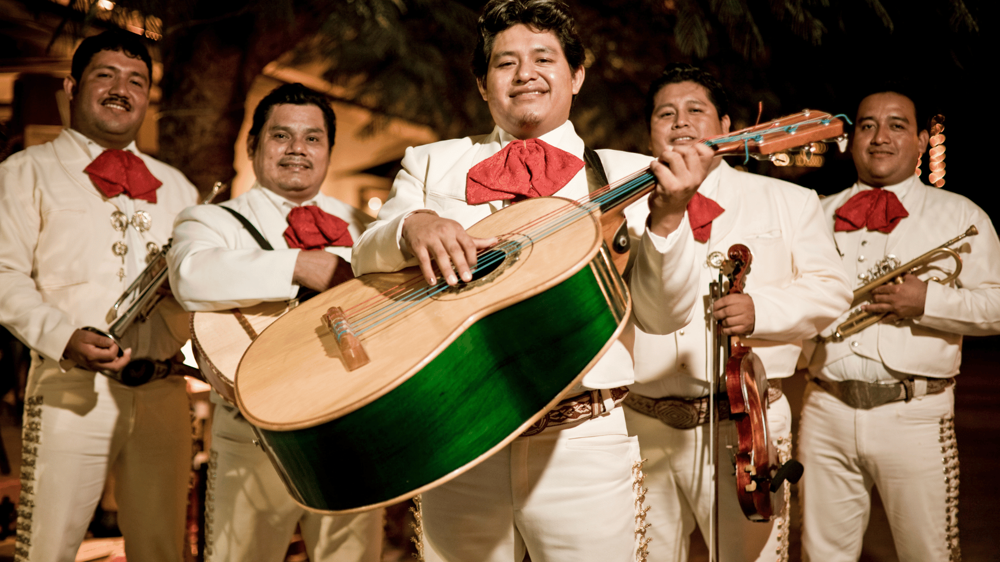 Mariachi zenét játszó mexikói együttes, kezükben gitárral, fehér ruhában és piros csokornyakkendővel