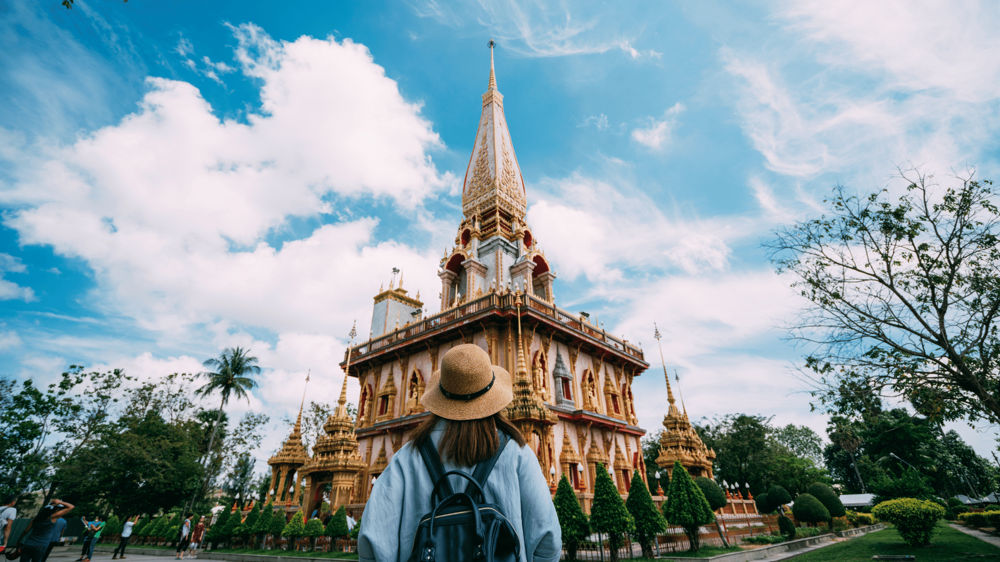 Egy lány Thaiföldre utazott, hátitáska van rajta és nézi a Thai templomot
