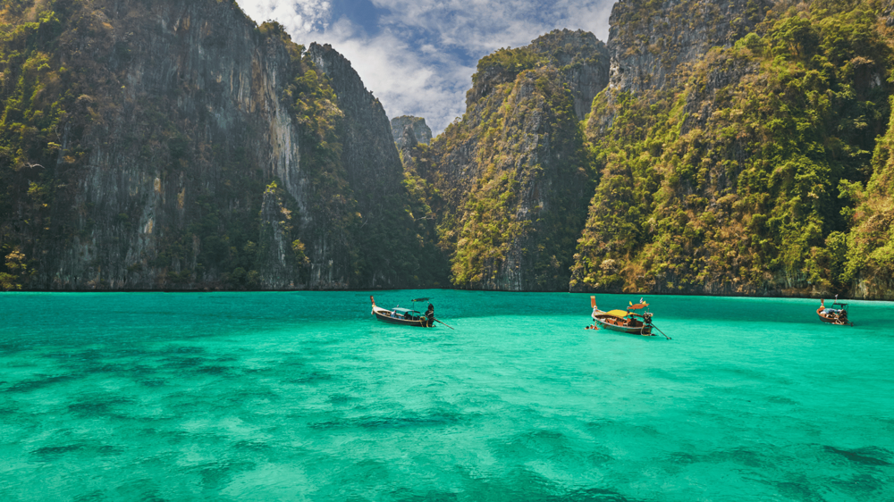 Krabi szigete, ahol a türkizkék tengeren csónakok eveznek és a háttérben a hatalmas hegyek látszanak