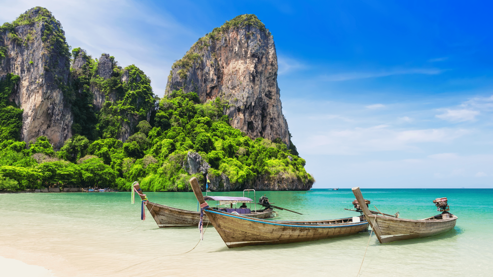Phuket szigetén két csónak áll, háttérben a hegyekkel és a kék tengerrel