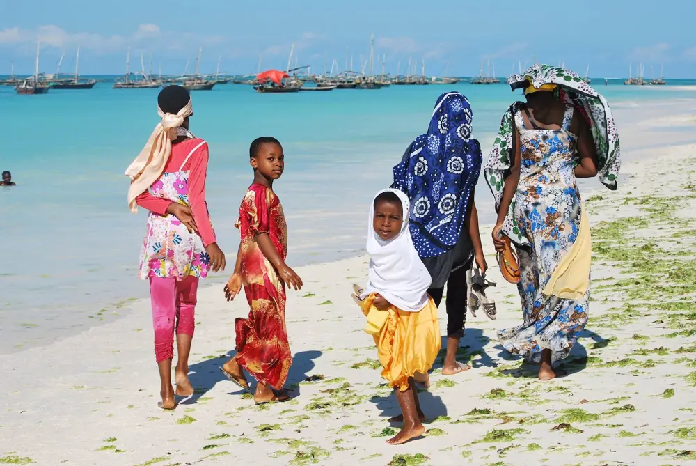 zanzibáriak a strandon sétálnak háttérben hajók